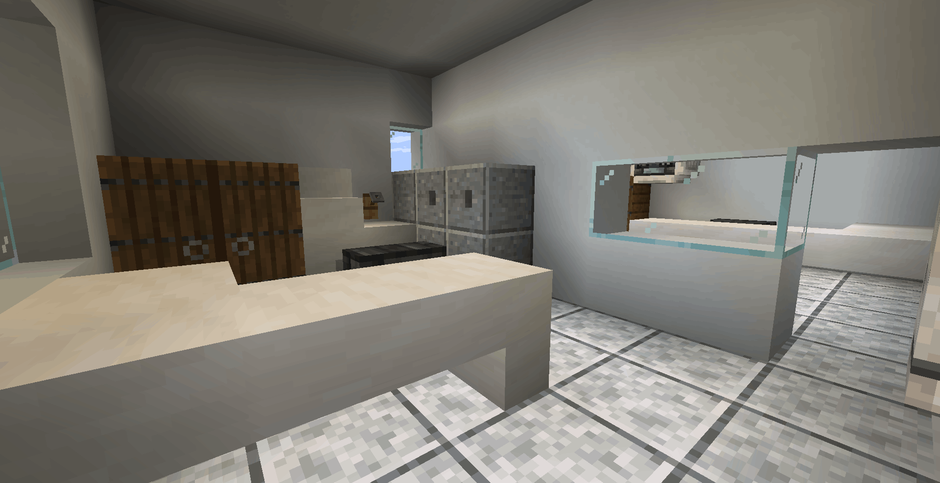 Interior de uma sala que parece ser a recepção ou secretaria. Possui um balcão em formato de "L" feito de blocos brancos lisos. Ao fundo, há armários de madeira, alguns blocos cinzas que simulam gaveteiros e uma janela de vidro que dá vista para outra sala.